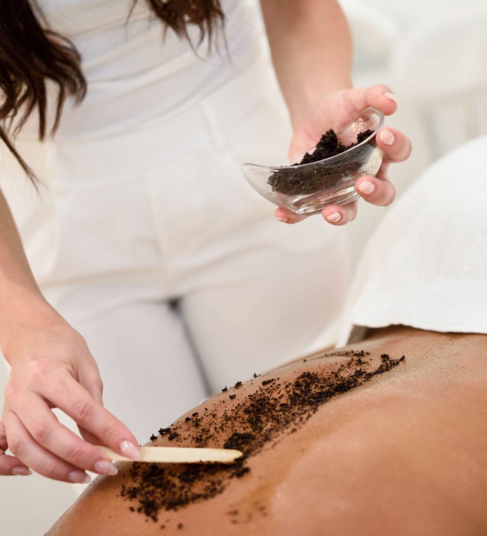 Woman cleans skin of the body with coffee scrub in spa wellness center. Beauty and Aesthetic concepts.