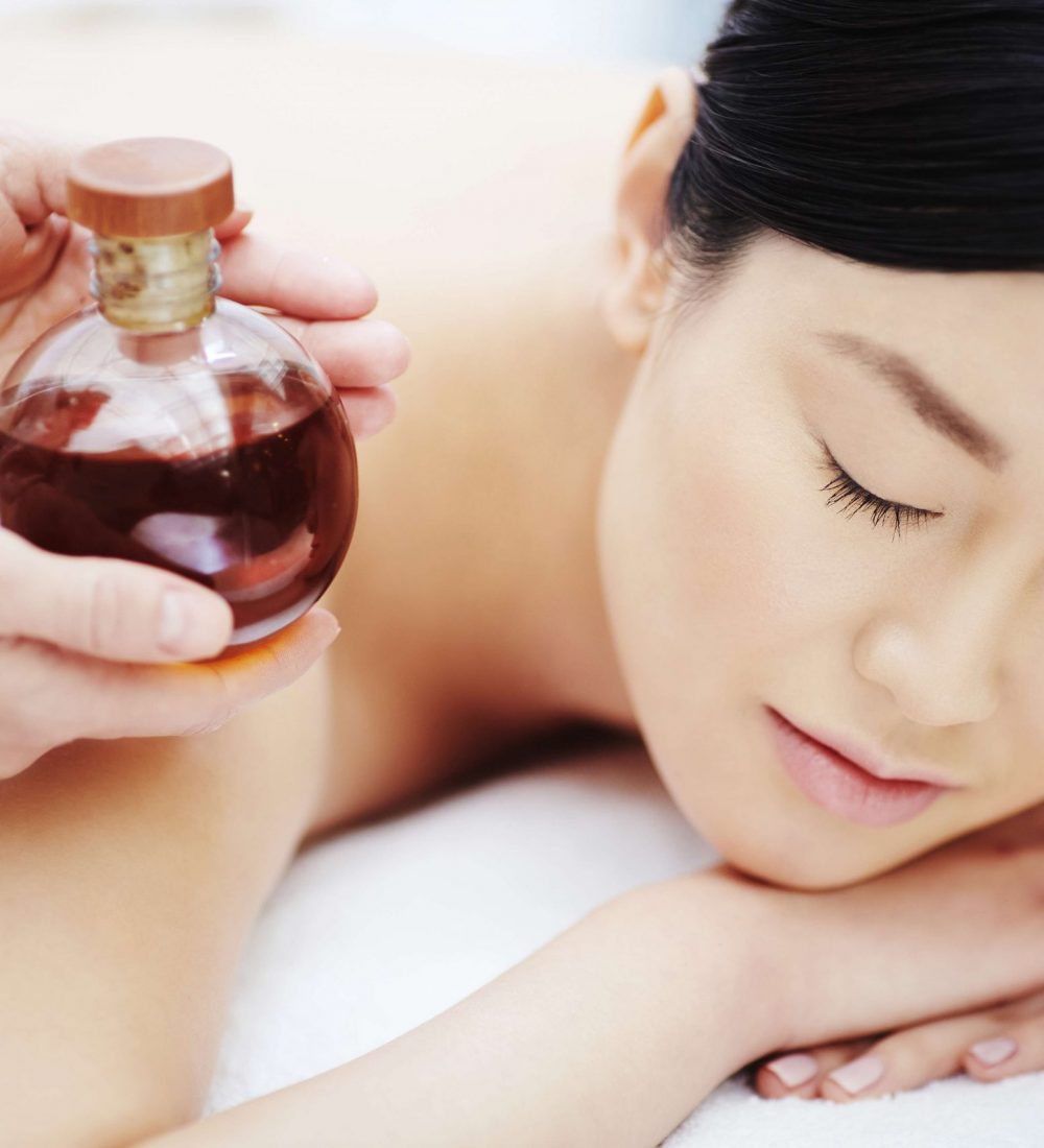 Bottle of massage oil in hands of beautician by relaxed girl